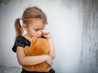 young girl with brown stuffed animal wiping her eye of tears