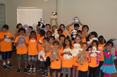 group of children predominantly wearing orange shirts with little hugs teddy bears donated to them