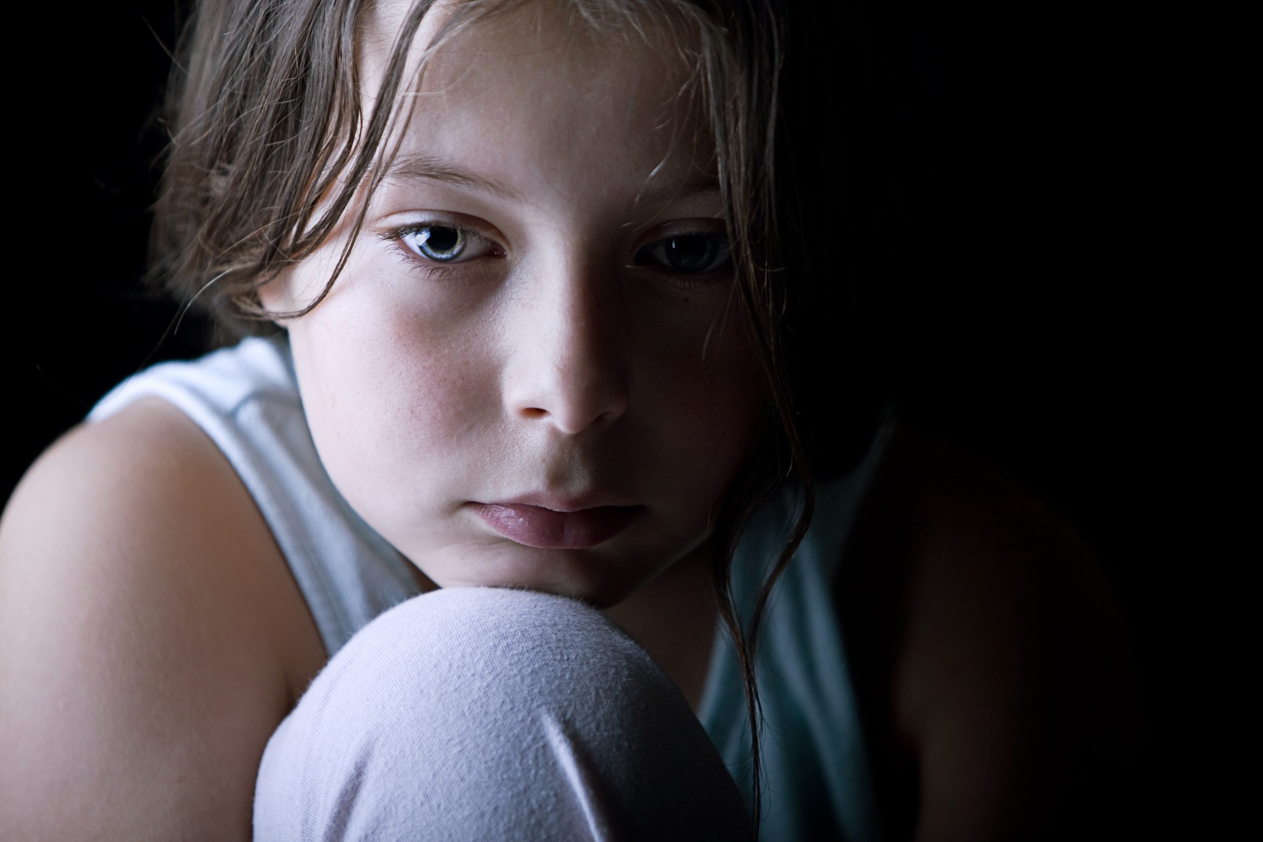 portrait of young child looking sad, head against knee