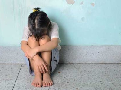 young girl head pointed down into lap sitting on floor with blue wall