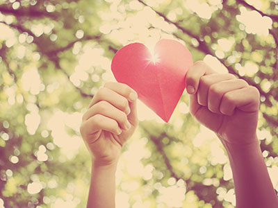 hands holding up red paper heart against forest background